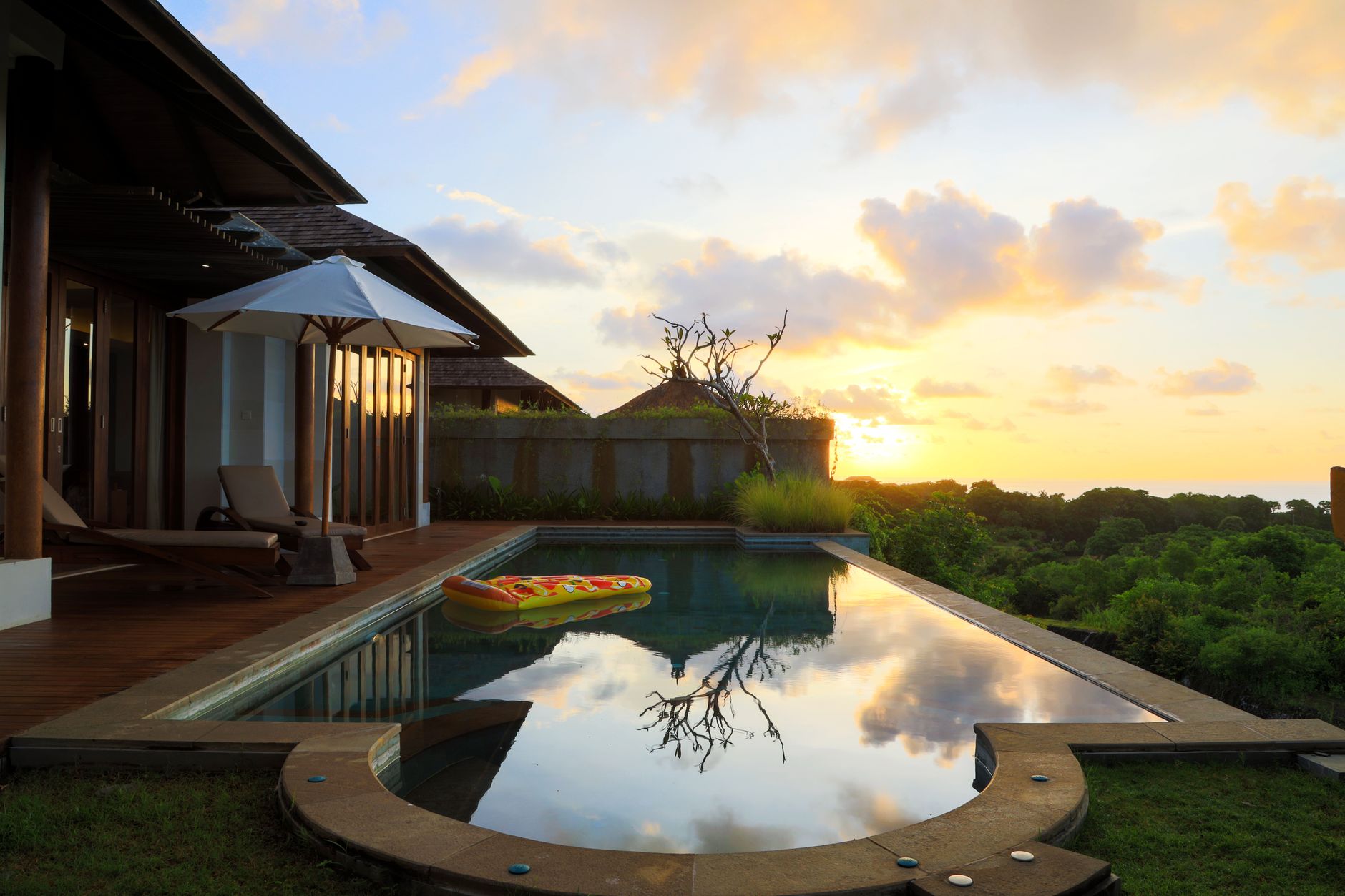 A serene view of a villa's infinity pool at sunset, with lush greenery and calm reflections