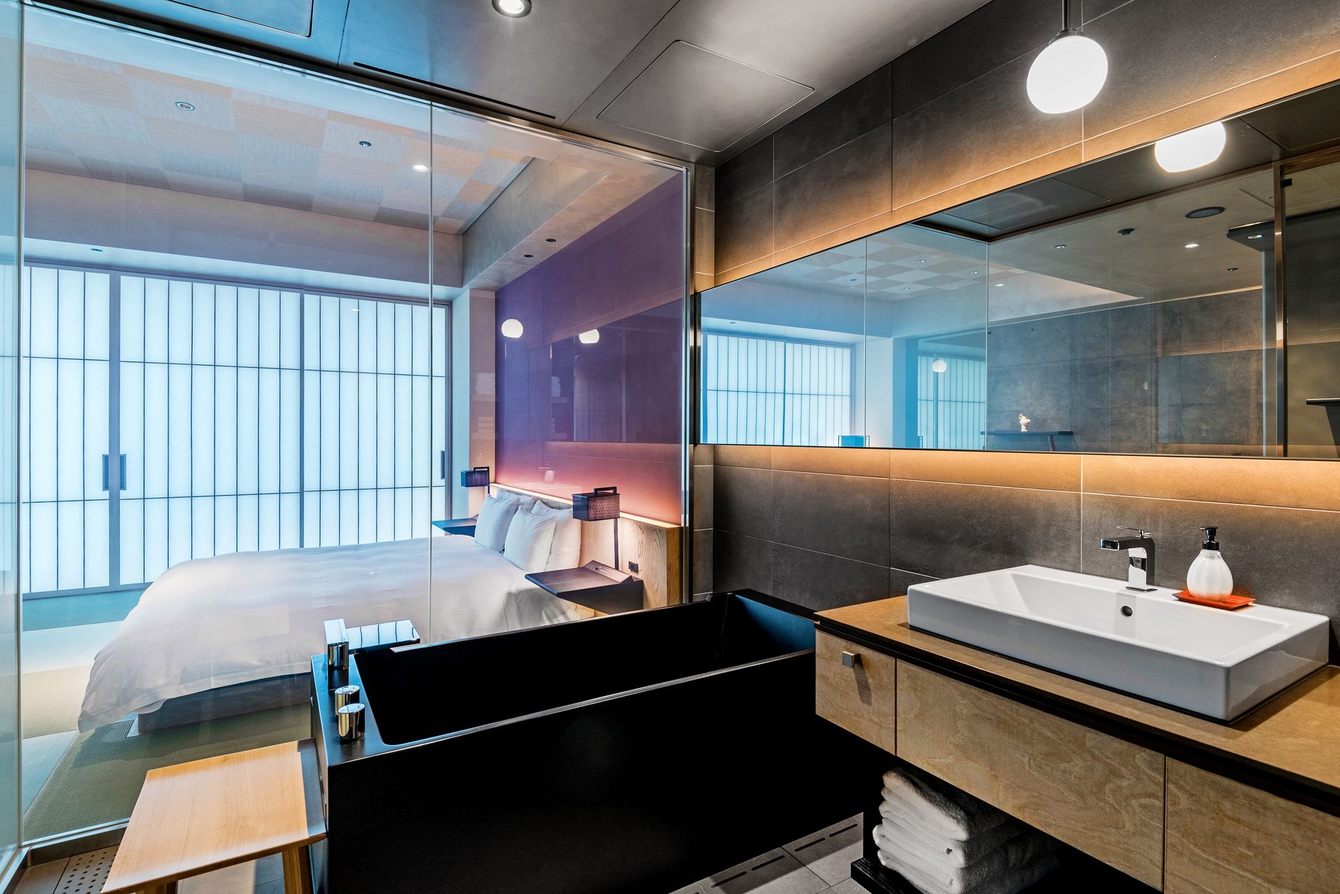Elegant hotel bathroom with a glass door view into a stylish bedroom, showcasing luxury interiors